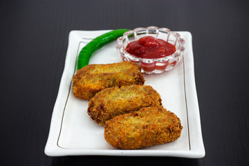 Three golden fried crisp cutlets served with tomato sauce or ketchup on white plate, prepare for iftar Ramadan. Wooden background. Selective focus. Copy space