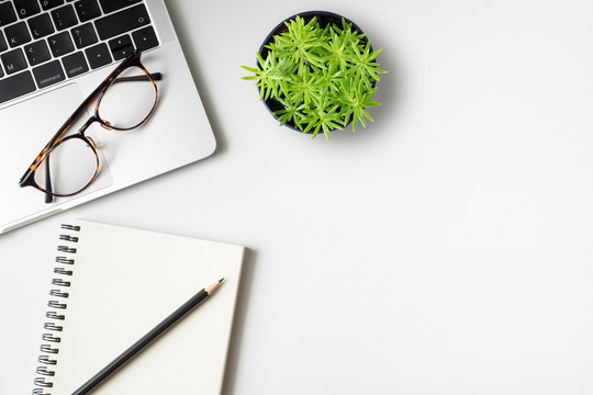 Top view desk with laptop computer notebook, pencil and plant potted on white background