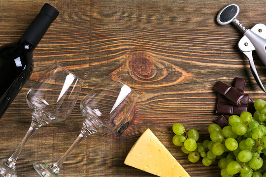 Red wine bottle, grape, cheese and glasses over wooden table. Top view with copy space