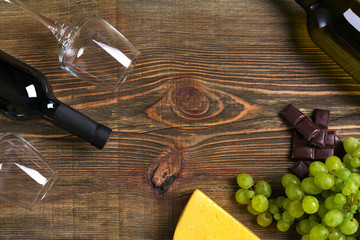 Red and white wine bottles, grape, cheese and glasses over wooden table. Top view with copy space