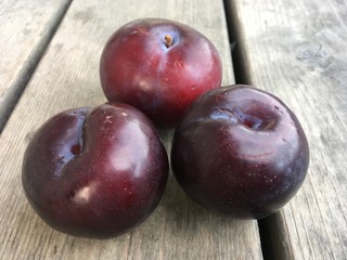Group of three plums sitting on a wooden table top