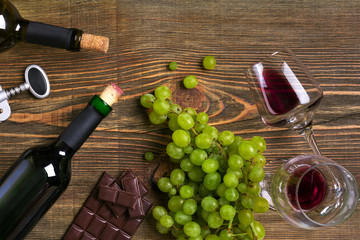 Obraz premium Red and white wine bottles, grape, chocolate and glasses over wooden table. Top view with copy space
