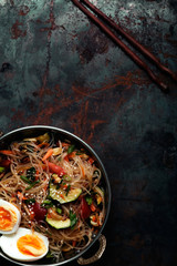 Spicy veggie wok: rice noodles with zucchini, onion and sesame. Asian styled lunch on metal textured background. Vertical composition with copy space for text