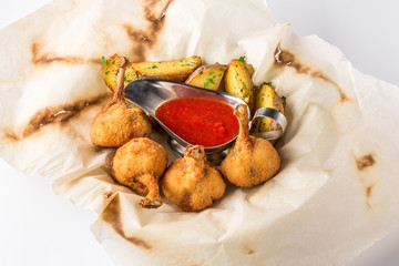 Fried chicken legs breaded and potato with sauce on a sheet of parchment