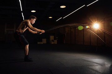 Fototapeta na wymiar Fitness man workout with battle ropes at gym. training exercise fitted body in club. Torso.