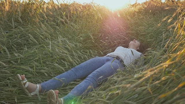 A young beautiful teen girl falls into a wheat field on a soft sunset.