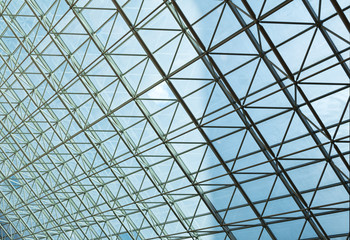 Contemporary steel structure and transparent glass roof revealing blue sky with light clouds