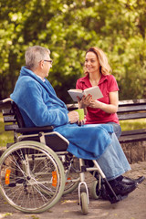 daughter reading book outdoor her disabled father in wheelchair.