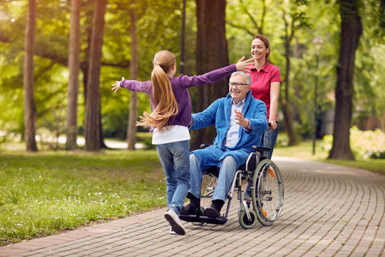 cheerful disabled grandfather in wheelchair welcoming his granddaughter.