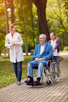portrait of elderly man on wheelchair with nurse and granddaughter outdoor.