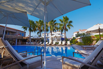 Relaxing pool at small hotel with umbrellas chaise-longue and surrounded with palms