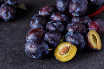 Plums, whole and slices on dark background.