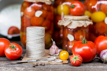 Tomato preserves in the jars, raw tomato fruits and seasonings on the wooden gray background