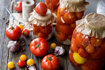 Tomato preserves in the jars, raw tomato fruits and seasonings on the wooden gray background