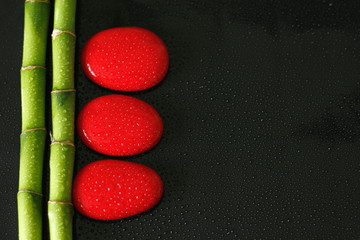 arrière plan noir avec branche de Bambou sur la gauche et galets zen rouge avec gouttes d'eau