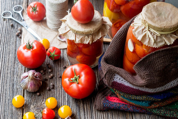 Tomato preserves in the jars, raw tomato fruits and seasonings on the wooden gray background