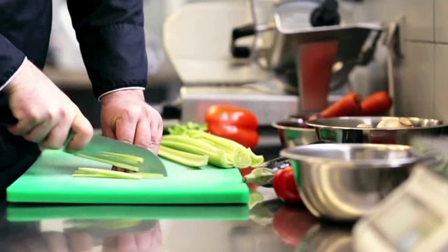 hands of male chef cook chopping celery in kitchen