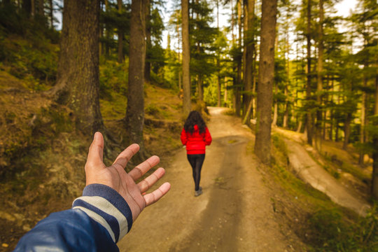 Man following a woman in red coat. Couple in the forest in a himalayan valley called Khajjiar in Himachal pradesh, India. Green trees and woods at sunrise. Perspective , POV picture