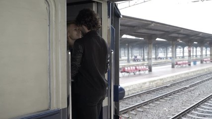 Young couple in love kissing and hugging goodbye in railway station before departing on rainy day