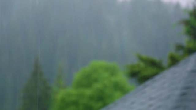 Heavy rain in mountain area and blurry wet grey roof of rural house. Focus at raindrops in foreground. Real time full hd video footage.