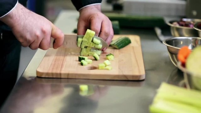 hands of male cook chopping cucumber in kitchen