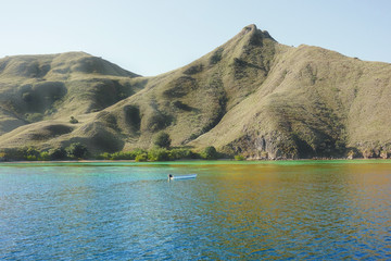 Small boat in front of coastline of mountains with green vegetation reflected  in blue ocean water at Labuan Bajo in Flores, Indonesia. © Eduard