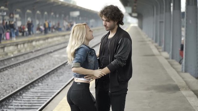 Happy couple kissing and walking hand in hand on railway station