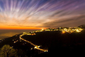  Clouds moving in fast during a beautiful sunset at Mcleodganj, Dharamsala, Himachal pradesh, India. Light Trails of Vehicles climbing up the mountain seen here. Purple golden yellow orange vibrant sk