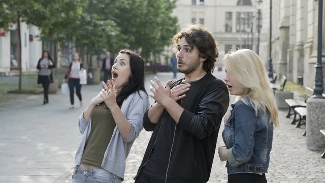 Three young group of friends girls and boy on the street reacting with shock seeing something amazing and scary