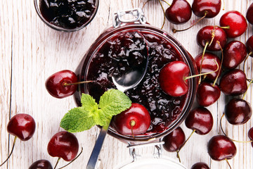Jar of cherry jam, sour cherries and spoon on white wooden background
