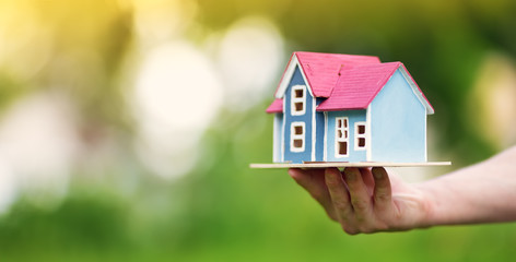man hands holding wooden house on the grass