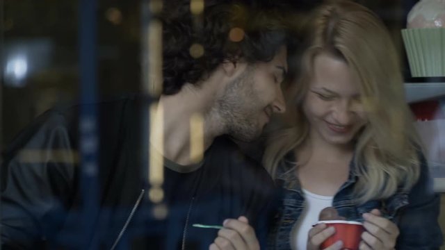 Young man playing a joke on his girlfriend while eating ice cream in a sweets candy shop