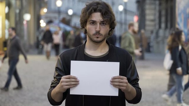 Determined young man holding a blank paper banner on the street with copy space for text