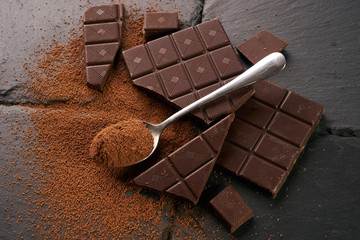Silver spoon with cocoa powder and dark chocolate on dark slate table