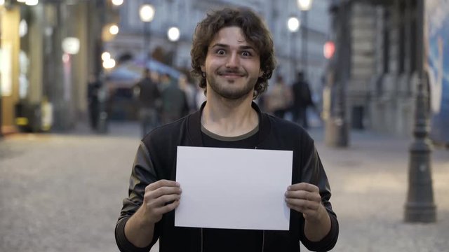 Happy smiling teenage man holding a blank copy space banner on the street in the city