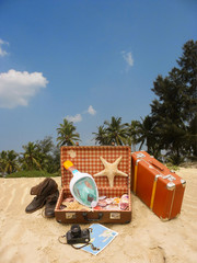 A vintage suitcase on a sandy beach, in it seashells and a snorkel mask are all that you expect to see on vacation.