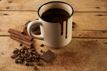 Vintage mug of hot chocolate drink with cinnamon sticks coffee beans anise and piece of chocolate on old wooden rustic table with copy space.