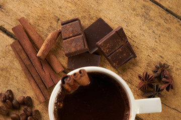 Top view of a mug of hot chocolate cinnamon sticks, coffee beans and broken dark chocolate bar on...