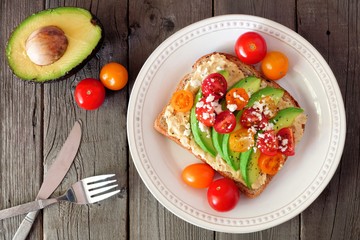 Avocado toast with hummus and tomatoes on plate, above scene on old wood background