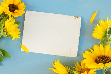 Sunflowers flowers on blue wooden table background, copy space on empty paper note, top view