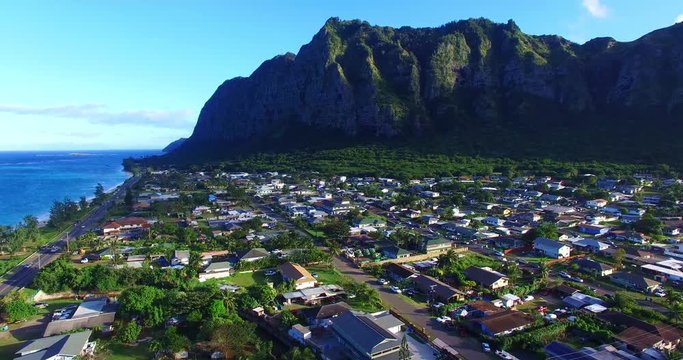 Highway Running Past Small Island Neighborhood in a Green Valley Surrounded by Imposing Green Mountains with Steep Cliff Walls - Aerial Footage on Oahu, Hawaii