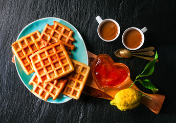 Breakfast with Belgian waffles, apricot jam and coffee on a black stone background