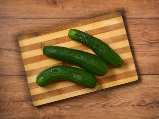 Pile of green cucumbers on wooden cutting board