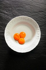 Yolks in a white bowl on a black stone background. Copy space