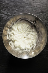 beaten egg whites in a large bowl. bakery products. Cooking. On a black stone table
