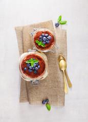 Homemade tiramisu cake traditional Italian dessert in glass jars on white stone table