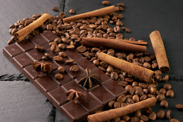 Coffee beans and cinnamon on a black stone background. Roasted arabica coffee beans pile with cinnamon stick and anise spice ingredients for fragrant coffee.