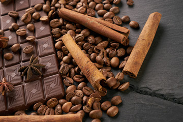 Coffee beans and cinnamon on a black stone background. Roasted arabica coffee beans pile with cinnamon stick and anise spice ingredients for fragrant coffee.