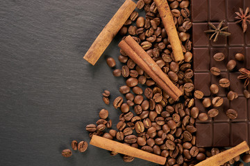 Close-up of roasted arabica coffee beans, dark chocolate bar and spices anise with cinnamon on dark stone background with copy space.