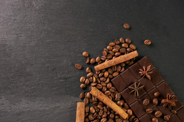Aromatic set of chocolate bar, arabica coffee beans, anise and cinnamon on dark stone background with copy space